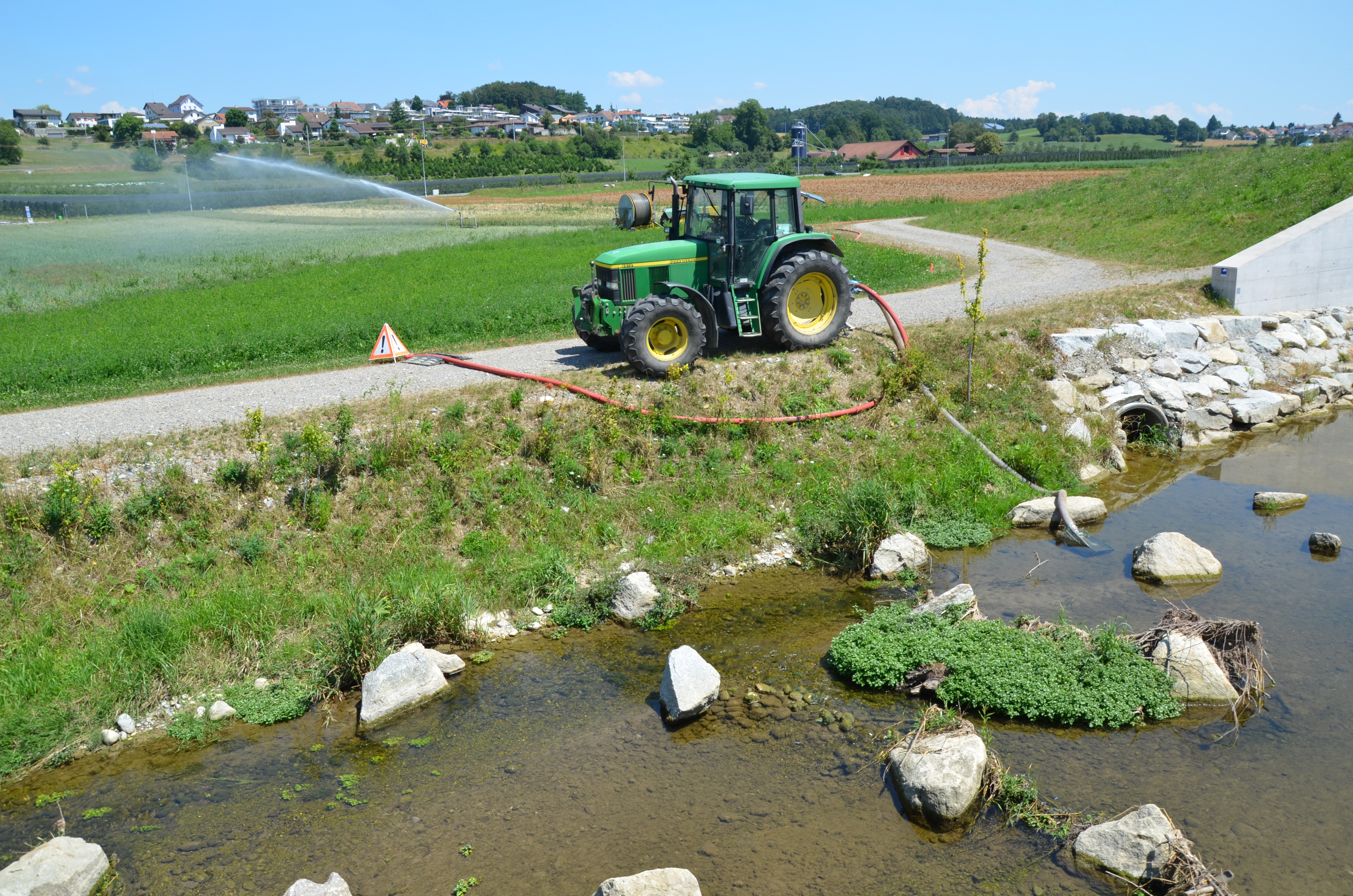 Ein Traktor pumpt Wasser aus einem Fluss.